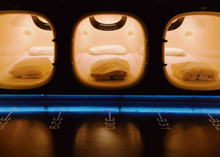 The rooms of a capsule hotel, showing small capsules with a bed, pillow, and sheet.